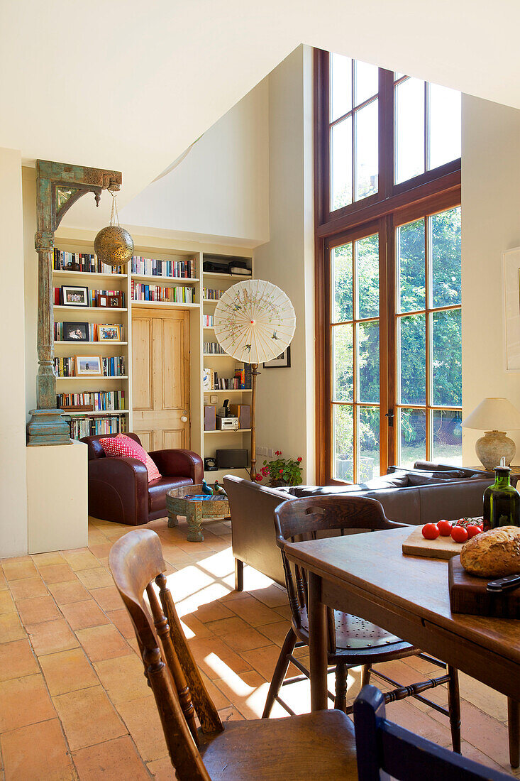 Open plan living room with wooden dining table and glass paned doors in Hackney home London England UK