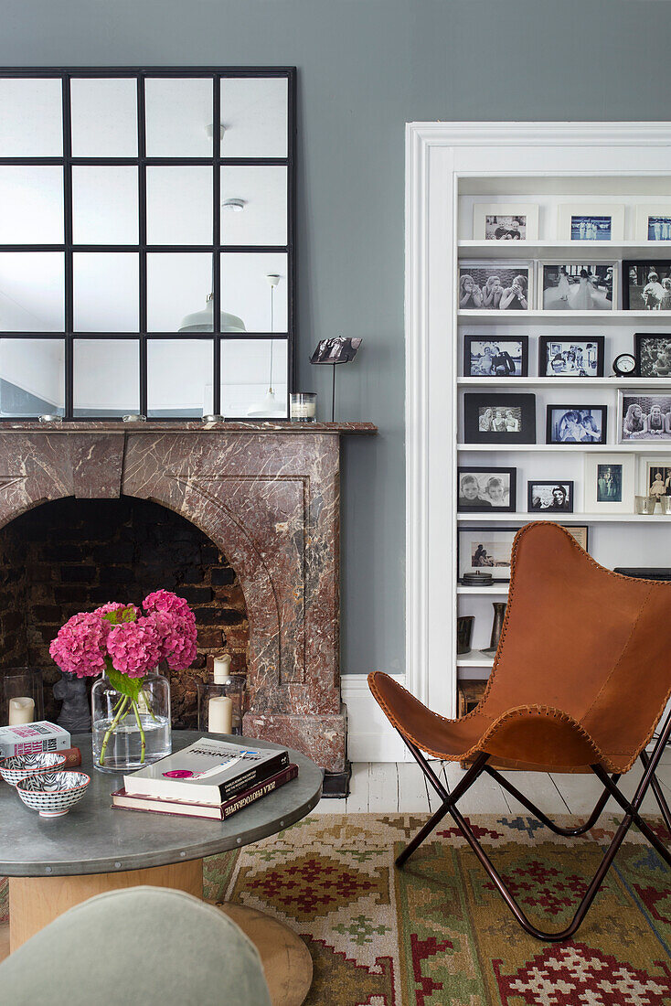 Leather butterfly chair with crittal mirror on marble fireplace and alcove of family photographs Southsea UK