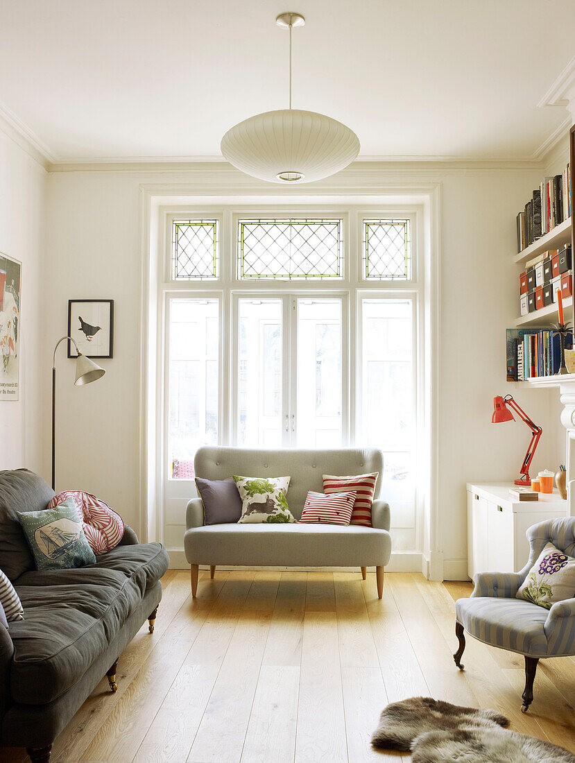 Sofas mit Kissen und sonnenbeschienenen Fenstertüren im Wohnzimmer eines Hauses in London England UK