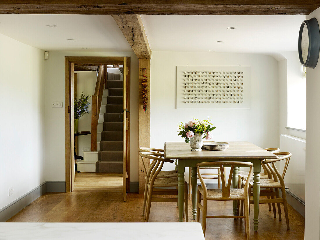 Roses in vase on table with chairs and view to staircase in West Sussex farmhouse, England, UK