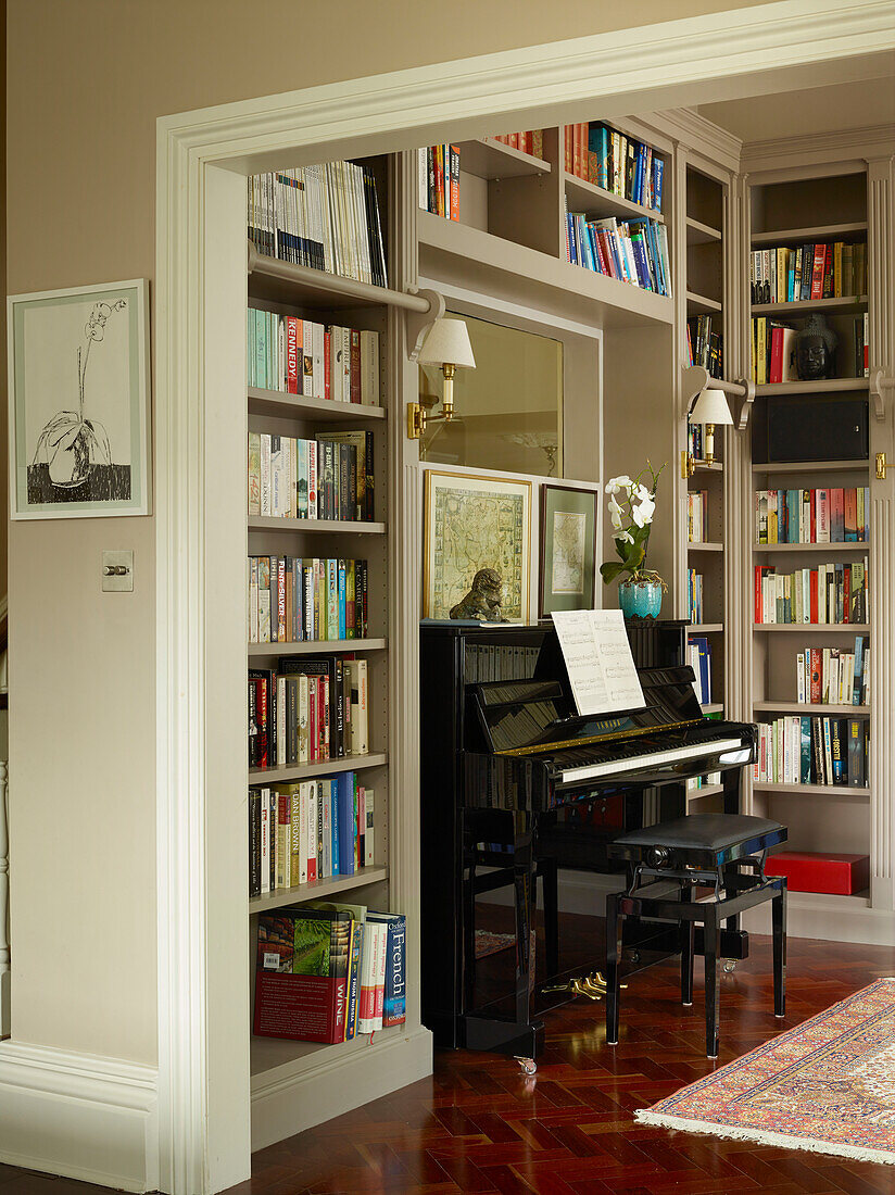 Piano and bookcases in library with polished parquet floor in London townhouse apartment, UK