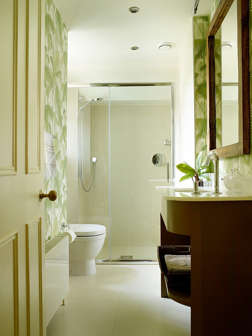 Shower cubicle with wood framed mirror above washstand in bathroom of London townhouse, UK