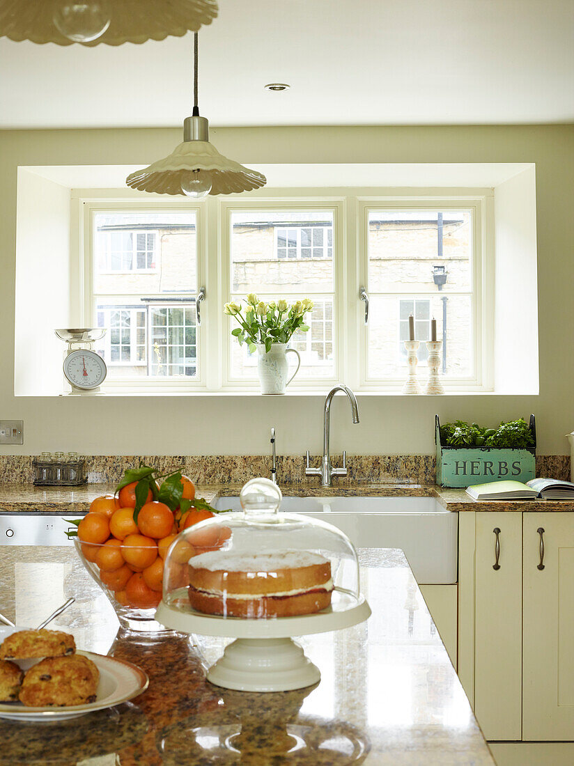 Sponge cake and satsumas on marble worktop in Oxfordshire kitchen, England, UK