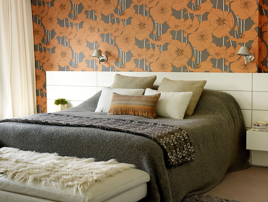 Graue Decke auf einem Doppelbett mit orangefarbener Blumentapete in einem Haus in London, Vereinigtes Königreich