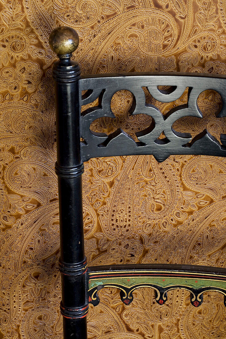 Geschnitzte schwarze Stuhllehne und braun gemusterte Tapete