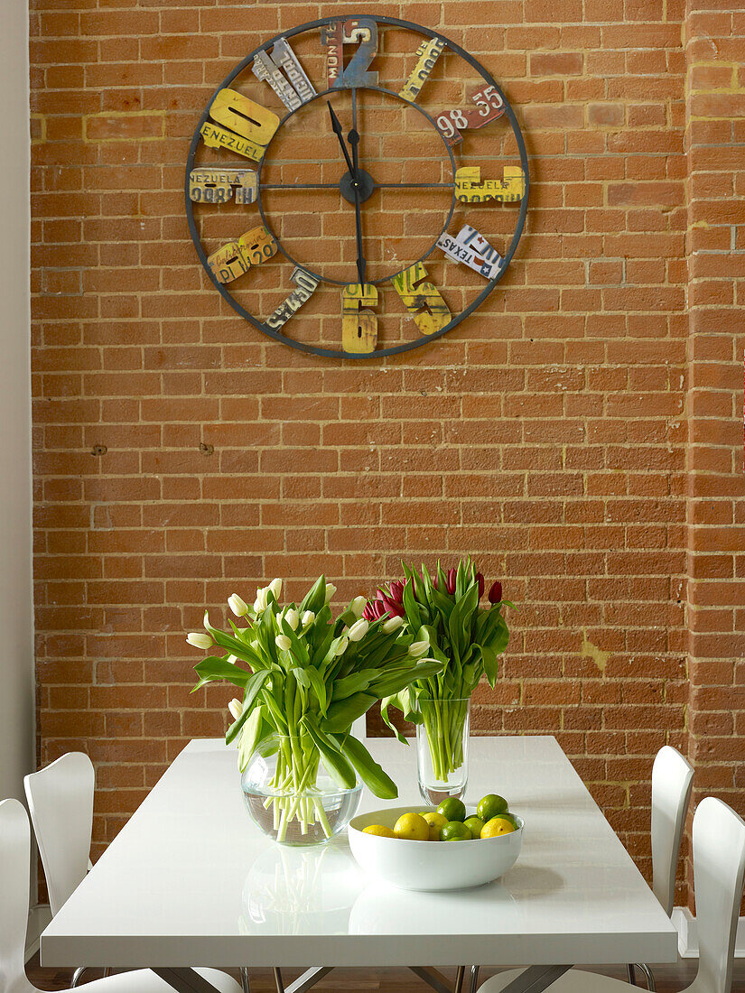 Metal clock made from salvaged materials above table with tulips in Ipswich warehouse conversion, Suffolk, England, UK