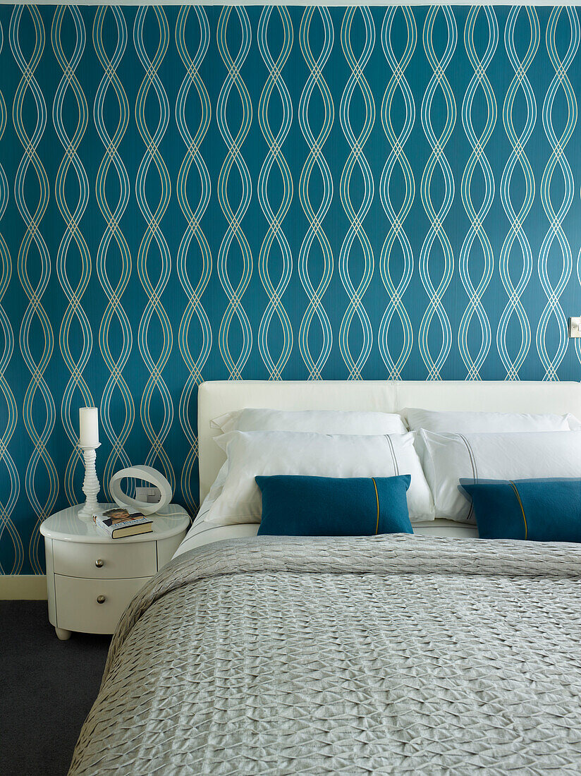 Blue patterned wallpaper above double bed with candle on side table in Manchester home, England, UK