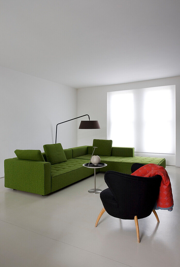 Lindgrünes Ecksofa und schwarzer Stuhl in weißem Interieur einer modernen Wohnung in London, England, UK