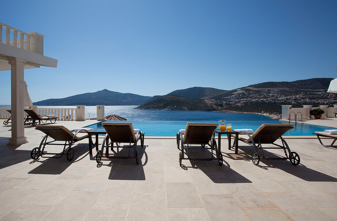 Vier Liegestühle am Pool einer luxuriösen Ferienvilla in der Türkei