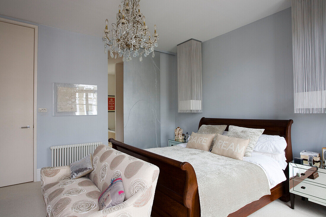 Wooden bed with sofa and mirrored bedside cabinets in London home UK