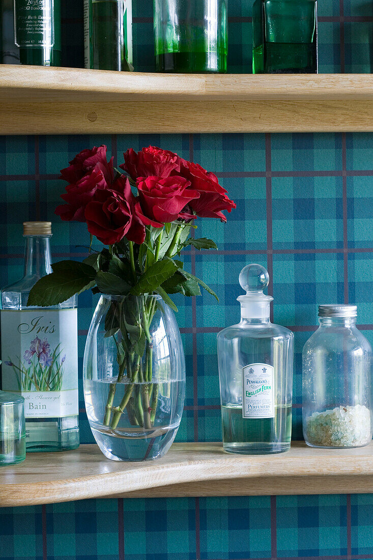 Vase of red roses on shelf with bottles set against turquoise checked wallpaper Suffolk UK