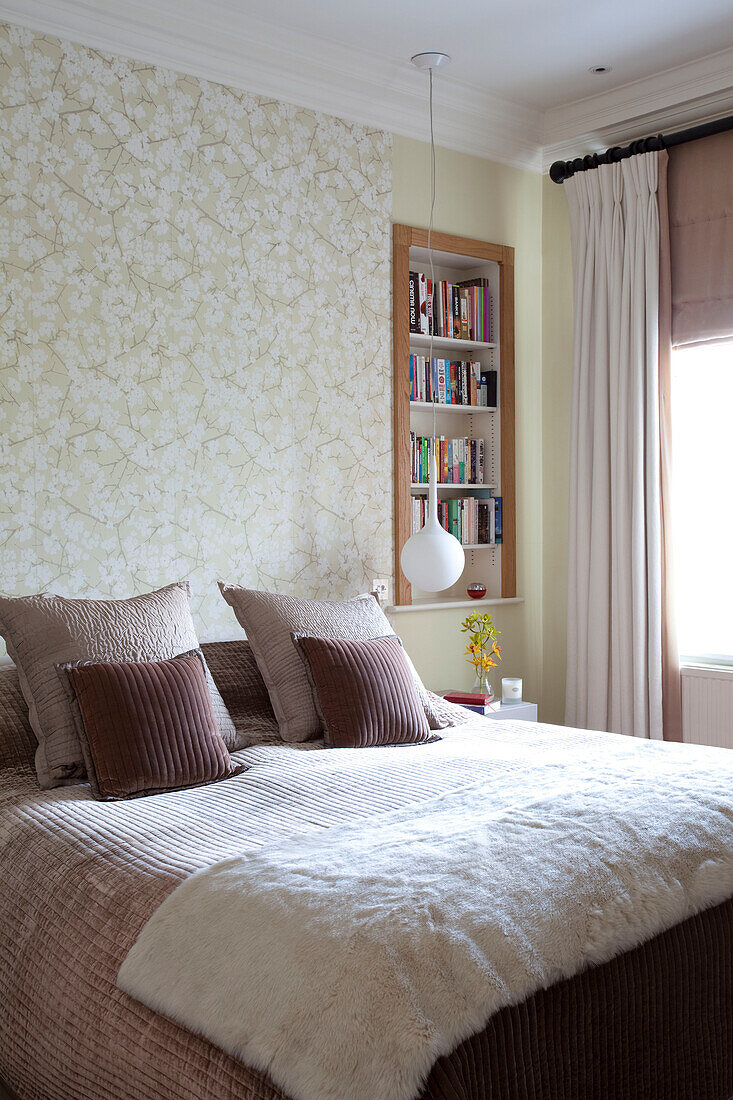 Cremefarbene Pelzdecke auf dem Bett in einem Zimmer mit eingelassenen Bücherregalen, modernes Haus in London, UK