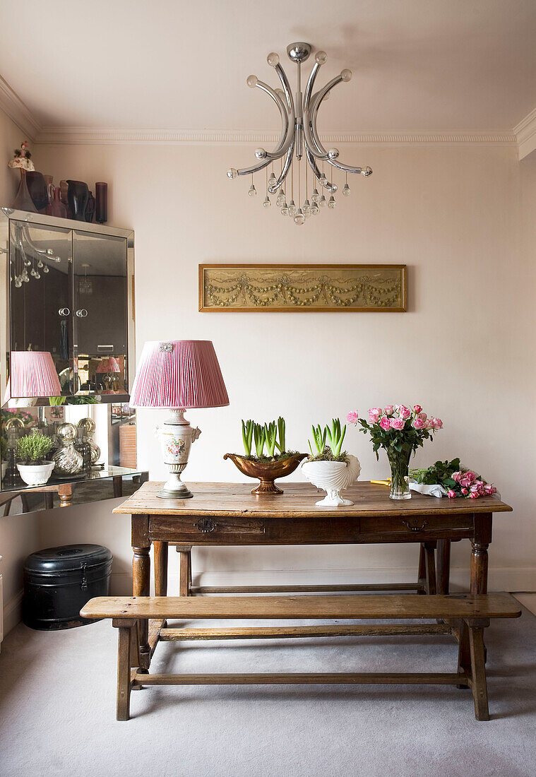 Crocus plants and cut roses on wooden table with mirrored corner cabinet London UK