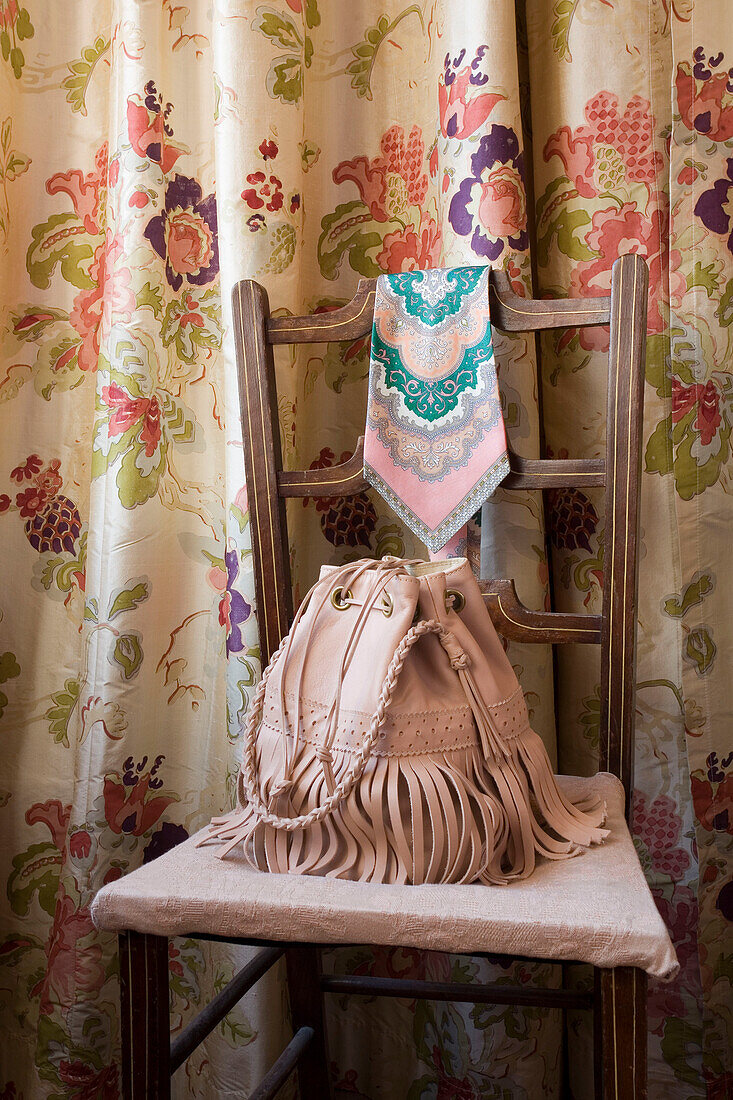 Pink leather handbag on chair with floral patterned curtains London UK