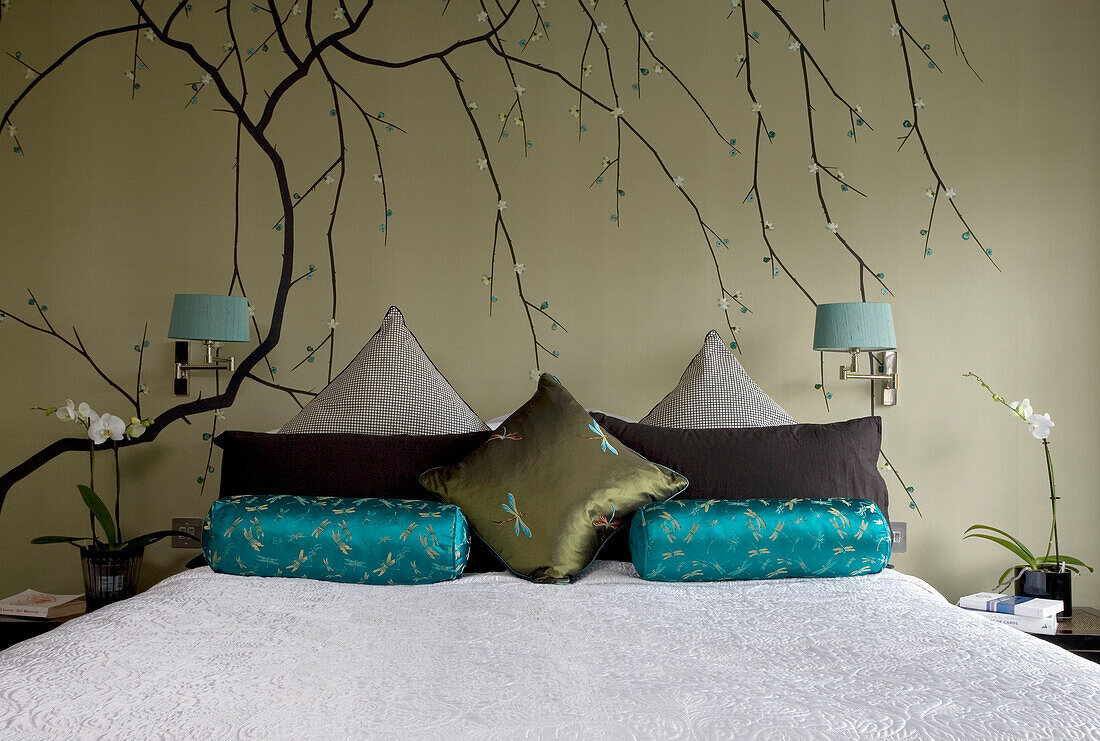 Oriental wall decor in bedroom with white quilted bed cover and upholstered cushions in contemporary London townhouse, England, UK