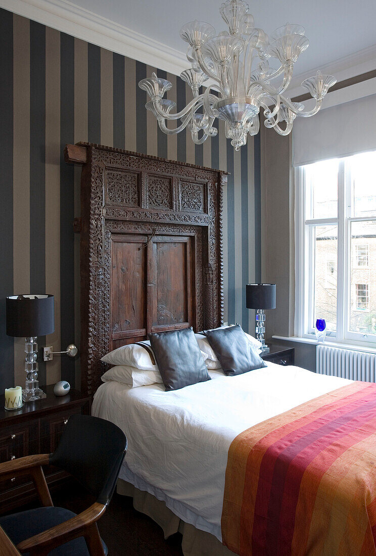 Striped wall paper and carved wooden headboard in London townhouse bedroom