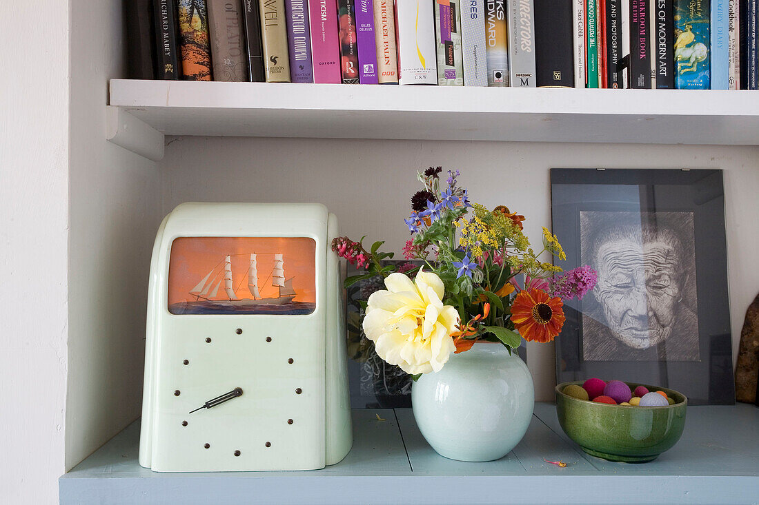 Nautical clock and cut wildflowers with book storage in Rye home, East Sussex, England, UK