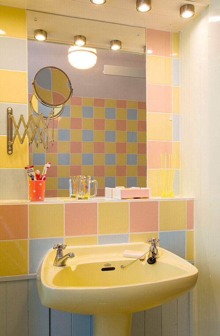 Multicoloured pastel tiles with yellow wash basin and shaving mirror in Rye home, East Sussex, England, UK