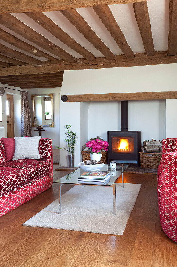 Red patterned sofa with glass topped coffee table in timber beamed house Kent UK