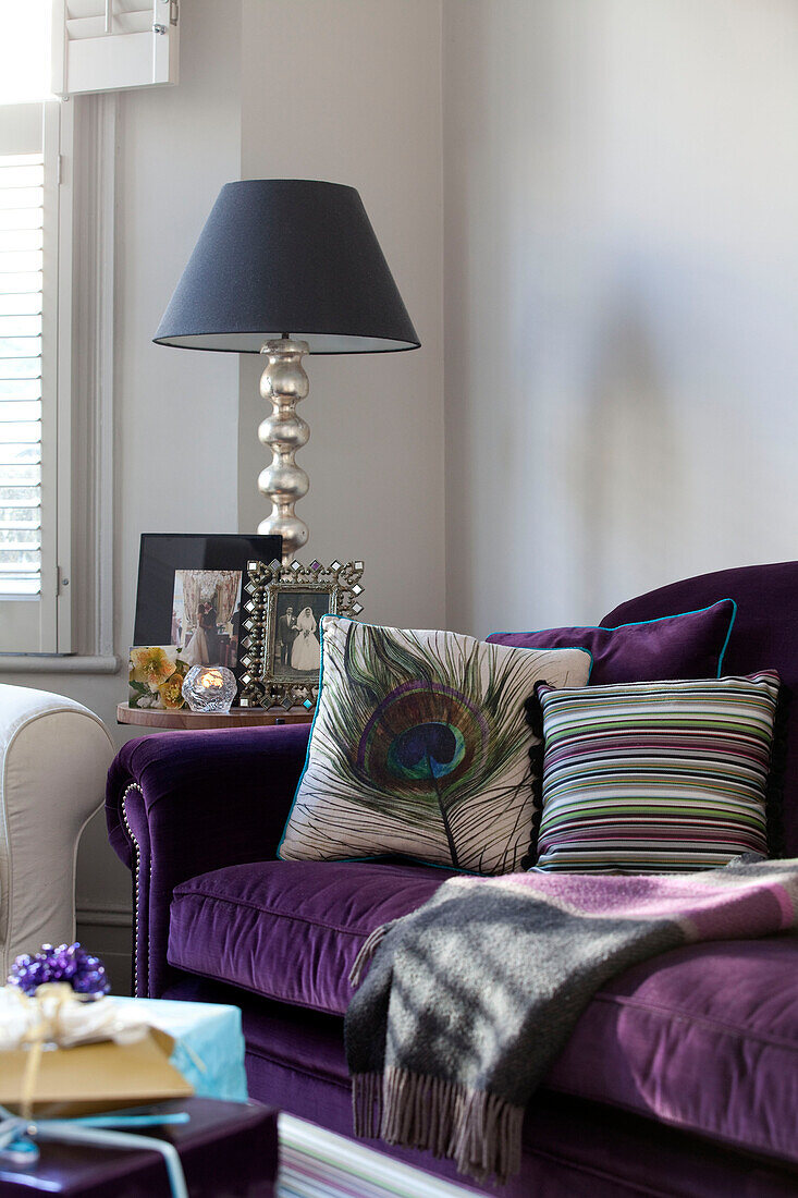 Peacock feather and stripey cushion on purple sofa in contemporary London home, UK