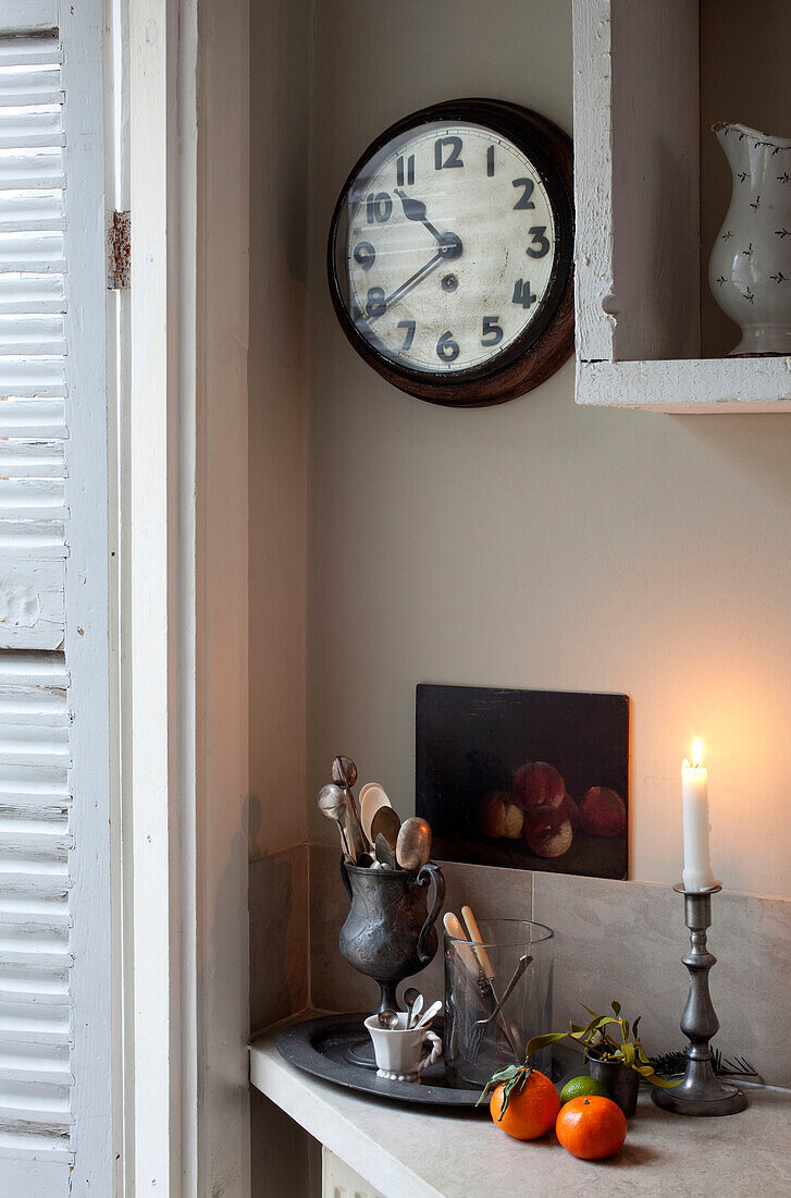 Beleuchtete Kerzen und Utensilien mit Wanduhr in einem Haus in London, England, Vereinigtes Königreich