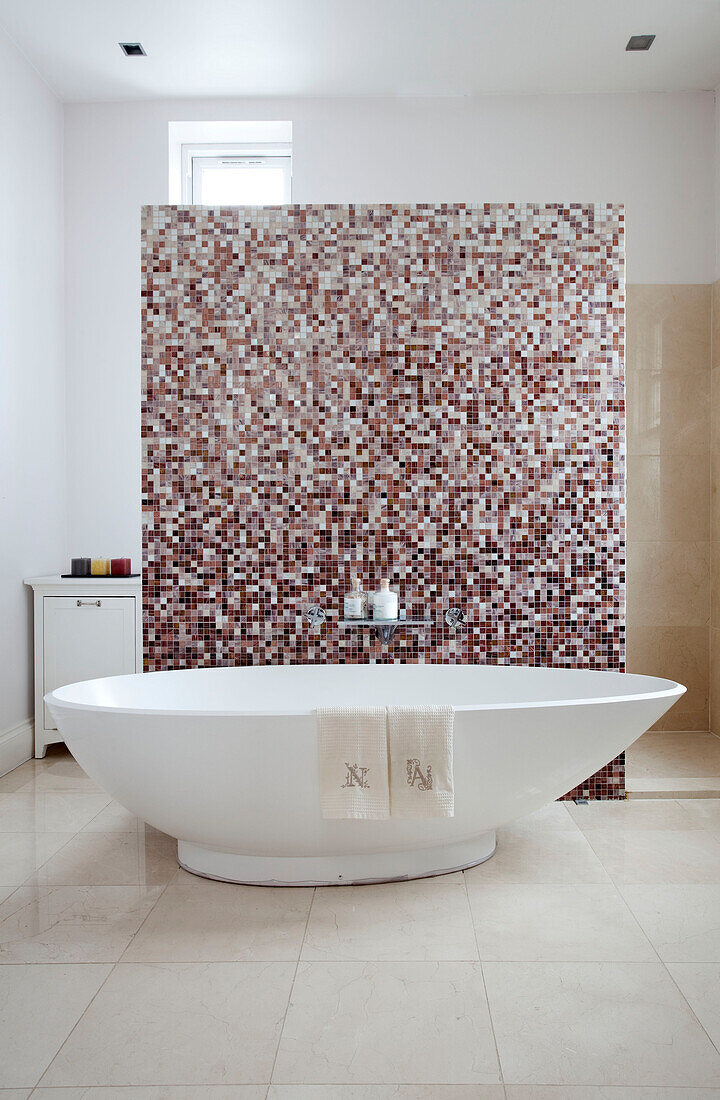 Freistehende Badewanne mit mosaikgefliester Trennwand in einem modernen Badezimmer in London, UK