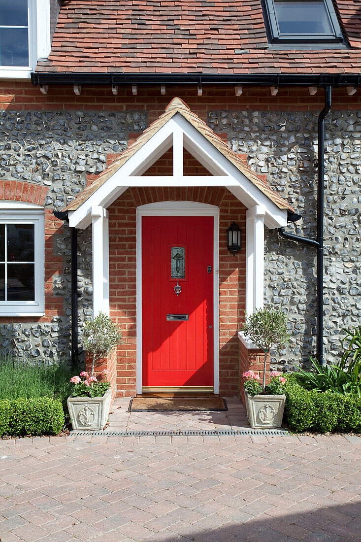 Red front door of stone Kent cottage with drainpipes in Kent, England, UK