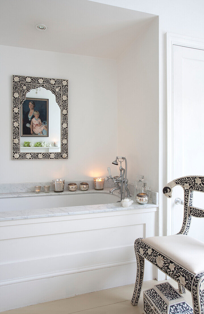 Silver candle holders on marble bath surround with co-ordinated mirror and chair frame in London home, UK