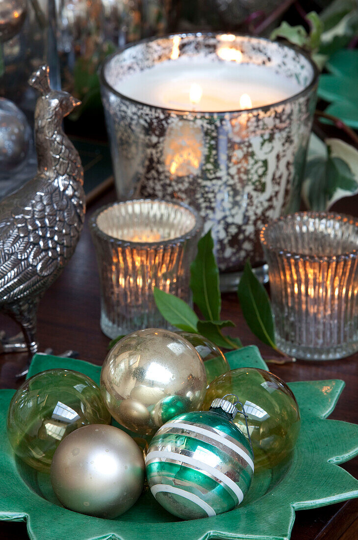 Lit candles and christmas baubles with silverware on dining table in London home, UK