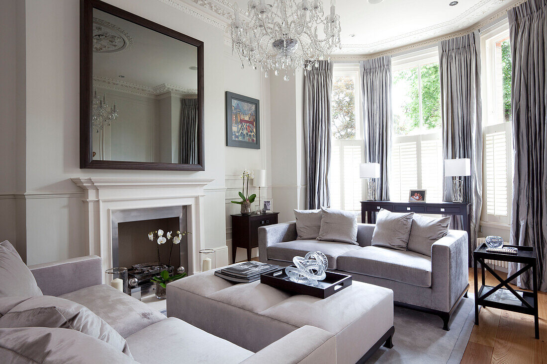 Large mirror above fireplace in classic living room with glass chandelier in London townhouse, UK