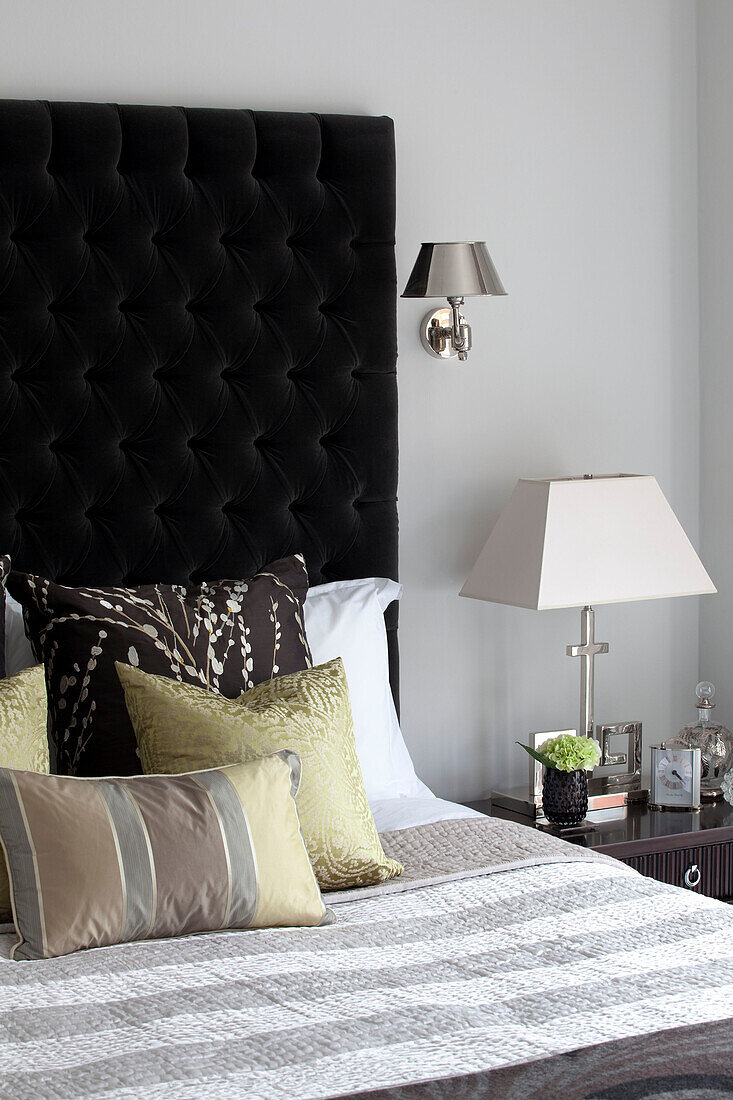 Verschiedene Kissen auf einem Doppelbett mit schwarzem Kopfteil in einer Londoner Wohnung, UK