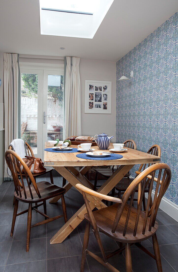 Esstisch und Stühle aus Holz mit blau gemusterter Tapete in einem Stadthaus in London, England, UK