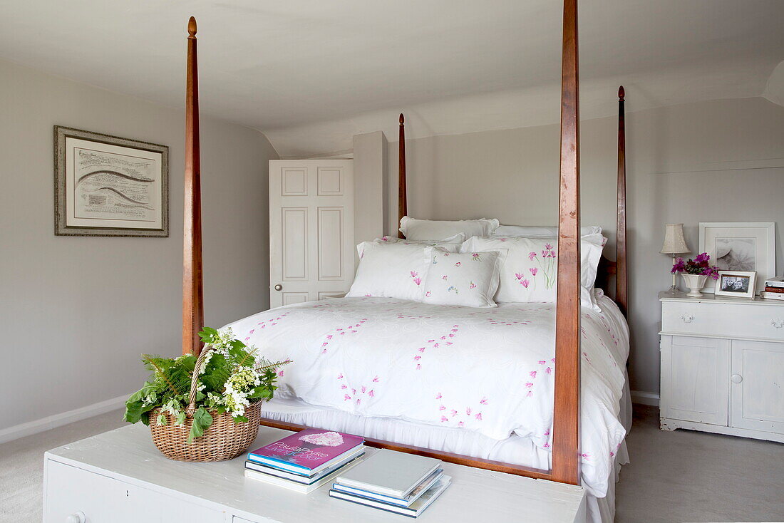 Wooden four poster bed with a basket of flowers in bedroom of Maidstone farmhouse, Kent, England, UK