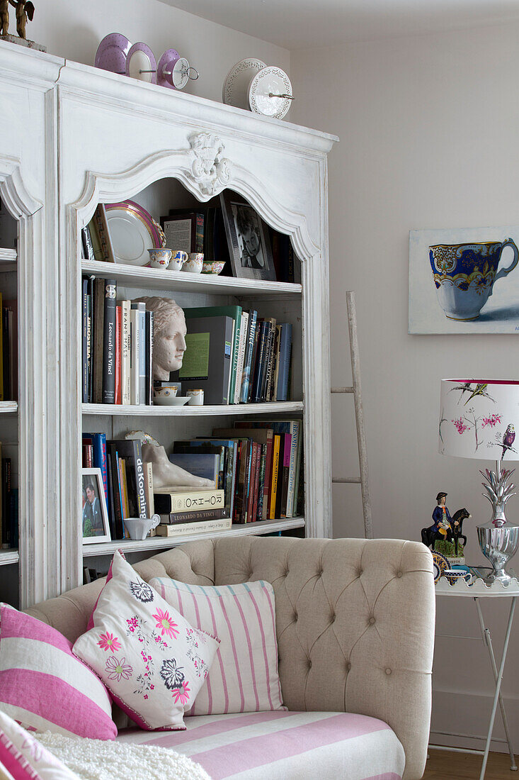 Cushions on buttoned sofa with bookcase in living room of Dulwich home London England UK