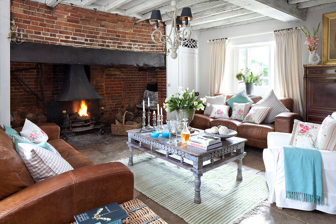 Braune Ledersofas und Couchtisch im Wohnzimmer mit offenem Kamin aus Backstein in einem Haus in West Sussex, England, UK