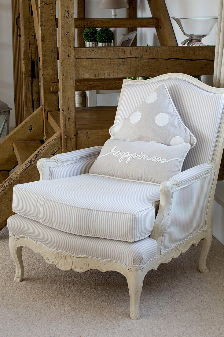 Upholstered armchair with 'happiness' cushion and wooden staircase in West Mailing home, Kent, England, UK