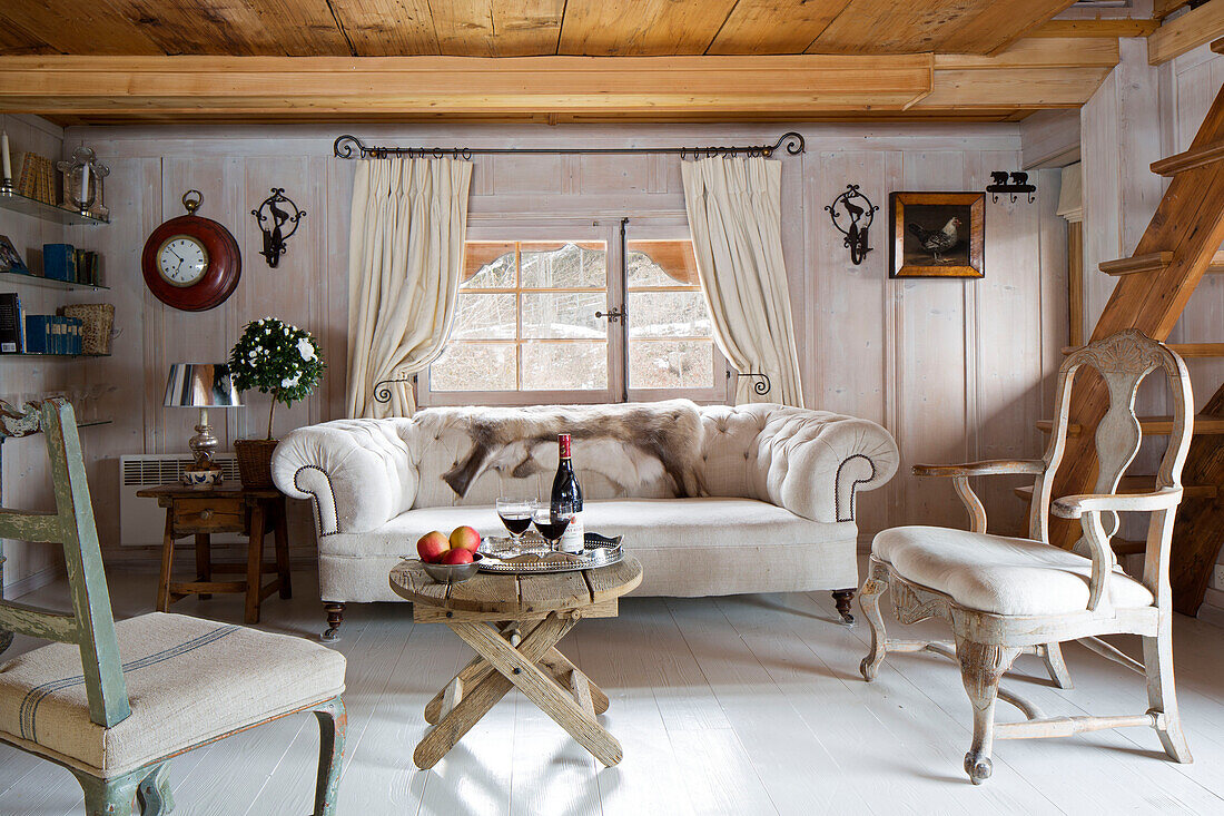 Cremefarbenes Sofa und Stühle mit Holztisch im Wohnzimmer eines Bergchalets in Chateau-d'Oex, Waadt, Schweiz