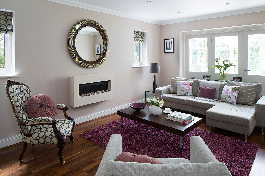 Pastellrosa Wohnzimmer mit rundem Spiegel und Ecksofa in einem Einfamilienhaus in London, England, UK