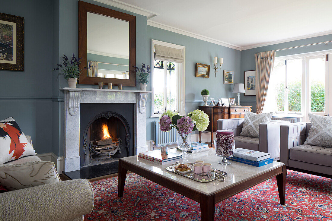 Holzgerahmter Spiegel über beleuchtetem Kamin mit Couchtisch und gemustertem Teppich in Berkshire, Wohnzimmer, England, UK