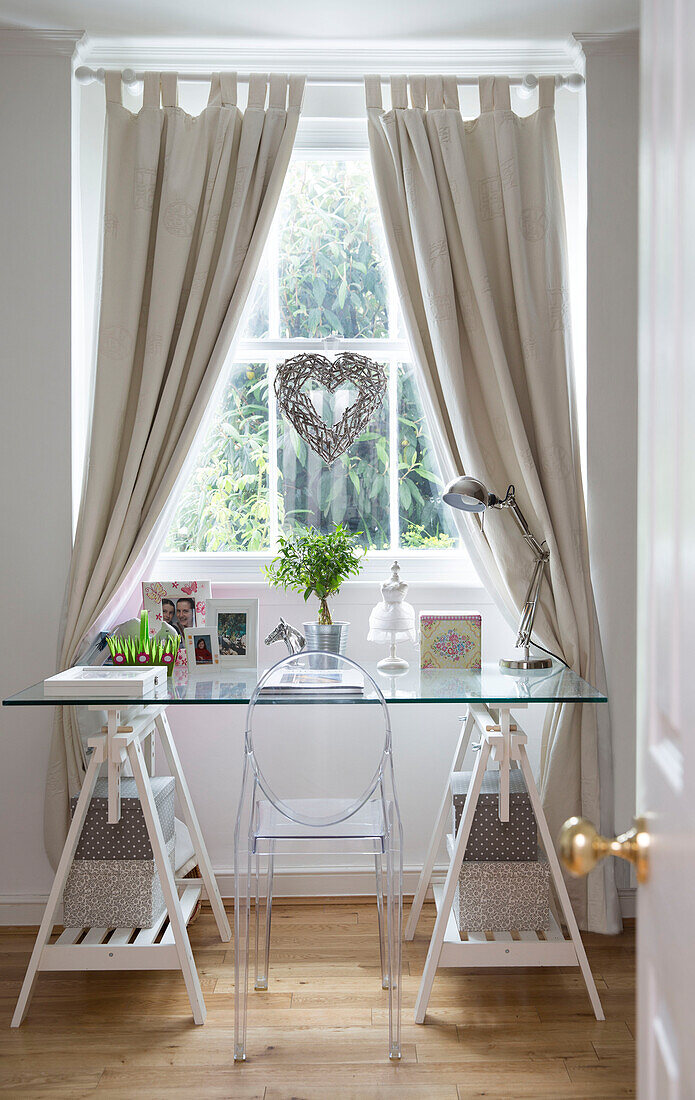 Wicker heart hangs in window above glass trestle table in London home, England, UK