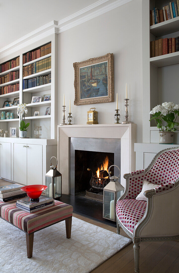 Spotted armchair and ottoman at lit fireside in living room of UK home