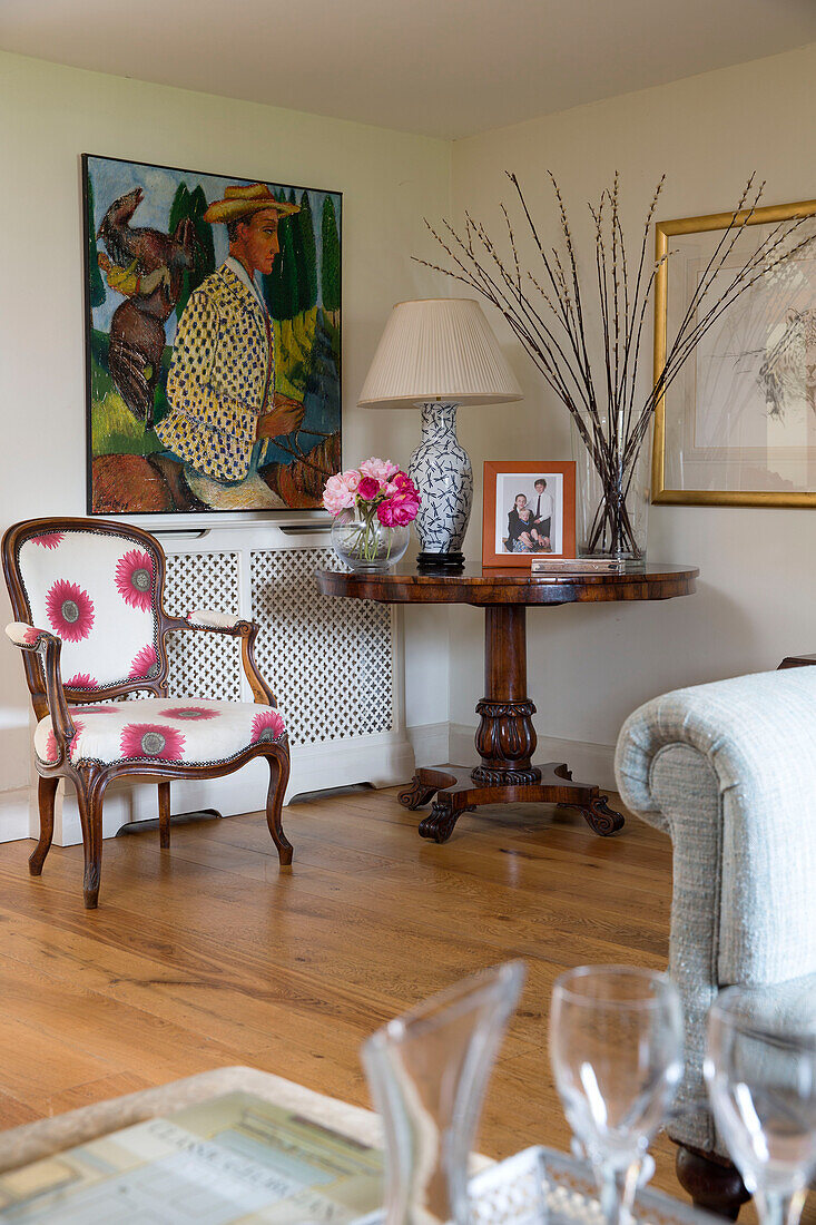 artwork with wooden pedestal table and upholstered armchair in Suffolk farmhouse,  England,  UK