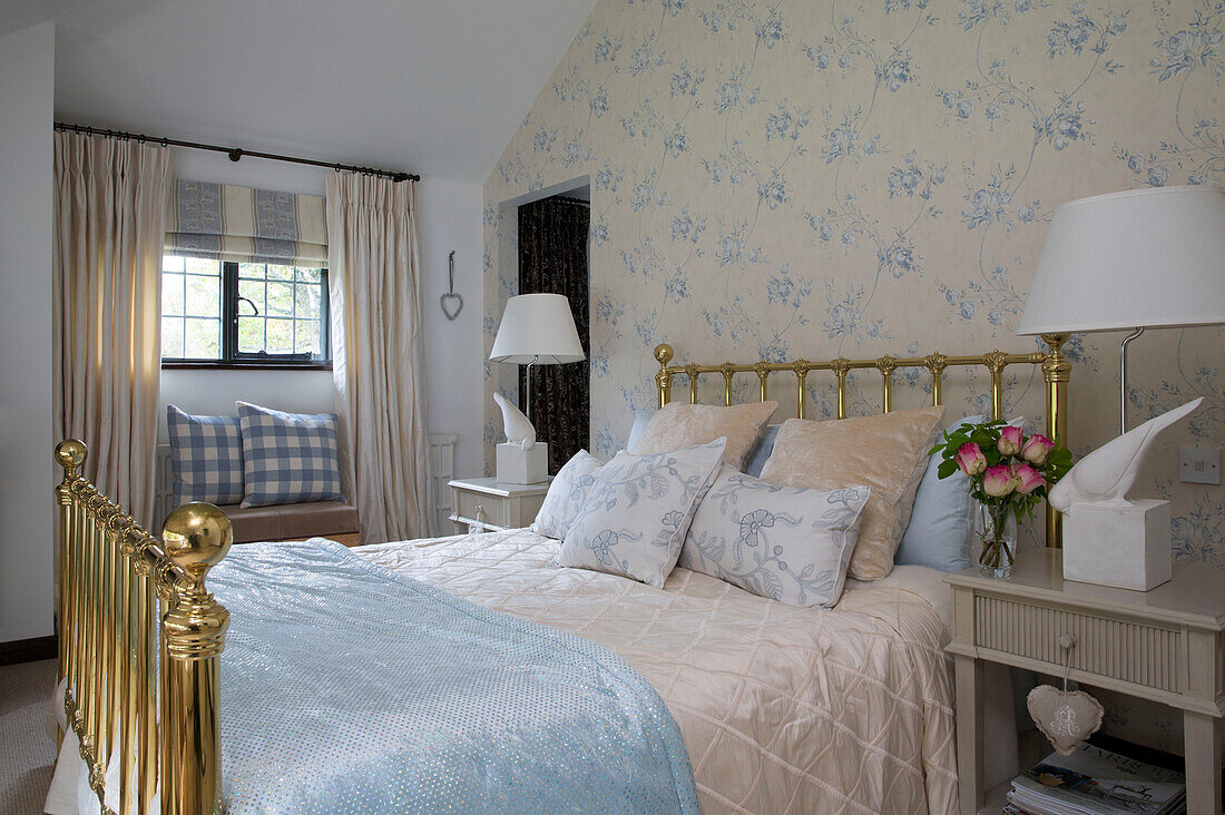 Messingbett mit hellblauer Mustertapete und Gingham-Kissen auf der Fensterbank in einem Cottage in Sussex, England, Vereinigtes Königreich