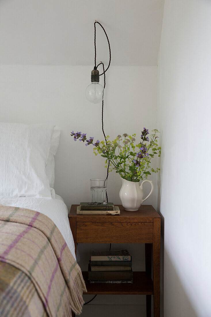 Lightbulb above cut flowers on wooden bedside table in Presteigne cottage Wales UK