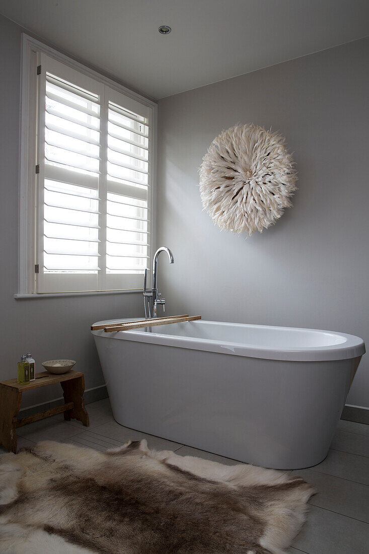 Gefiederter Kopfschmuck über der freistehenden Badewanne unter dem Fenster im modernen Badezimmer in Sussex, England, UK