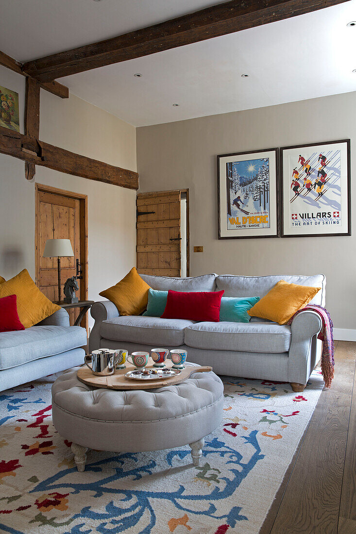 Cup on ottoman footstool with colourful cushions and framed prints in Surrey home,  England,  UK