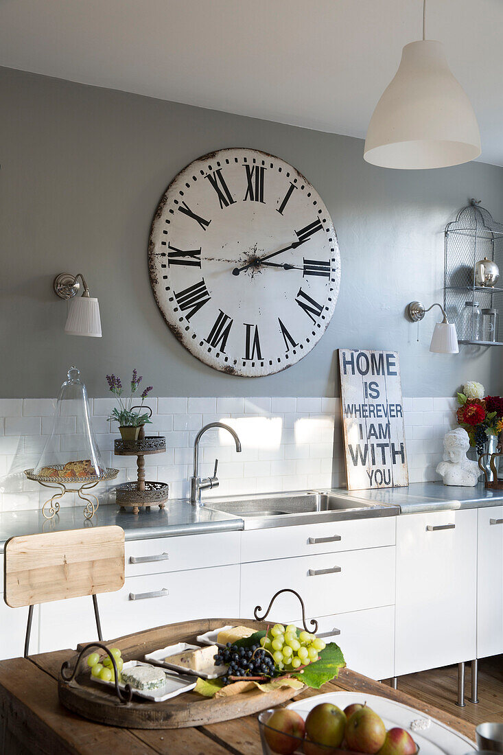 Large vintage clock above sink in Berkshire kitchen with cheeseboard,  England,  UK