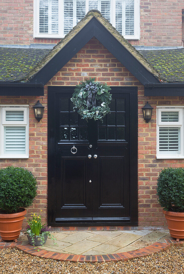 Christmas wreath above black front door of brick Chobham home   Surrey   England   UK