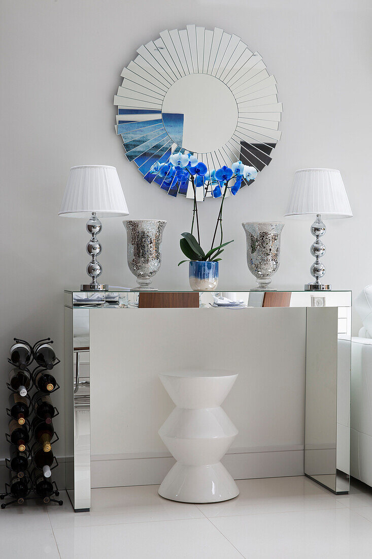 Pair of matching lamps with circular mirror and wine rack on mirrored console in contemporary London home   UK