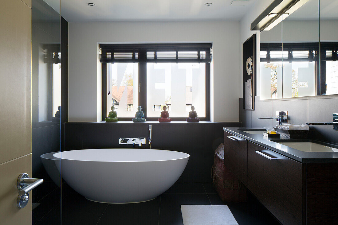Freistehende Badewanne am Fenster eines Badezimmers mit Doppelwaschbecken und Spiegelschränken in einem Haus in London, England, UK